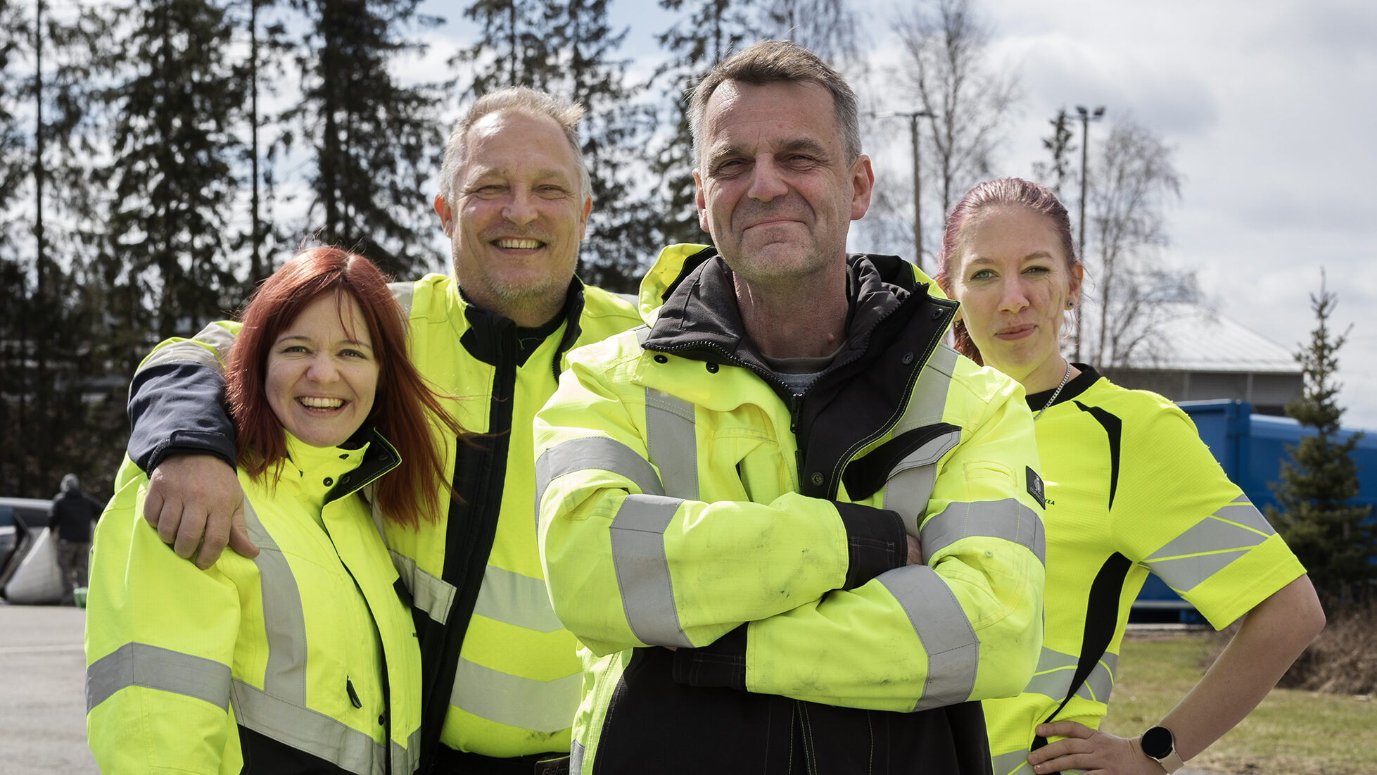 Kaksi naista ja kaksi miestä seisoo huomiovaatteet päällä ja katsovat iloisesti kameraan.