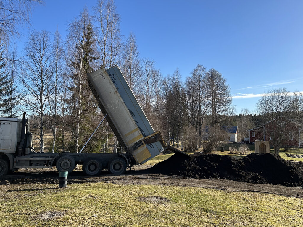 Kuorma-auto kippaa isoa multakuormaa omakotitalon pihalle. On vielä kevät.