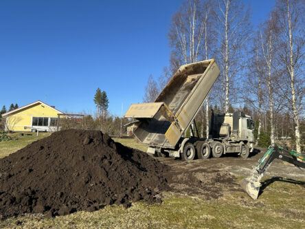 Kuorma-auto kippaa isoa multakuormaa omakotitalon pihalle. On vielä kevät.