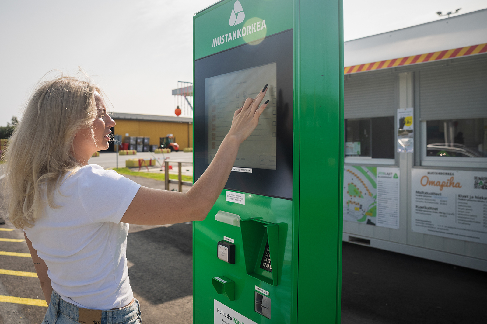 Nainen maksaa ostoksia automaatilla, takana näkyy infokoppi.