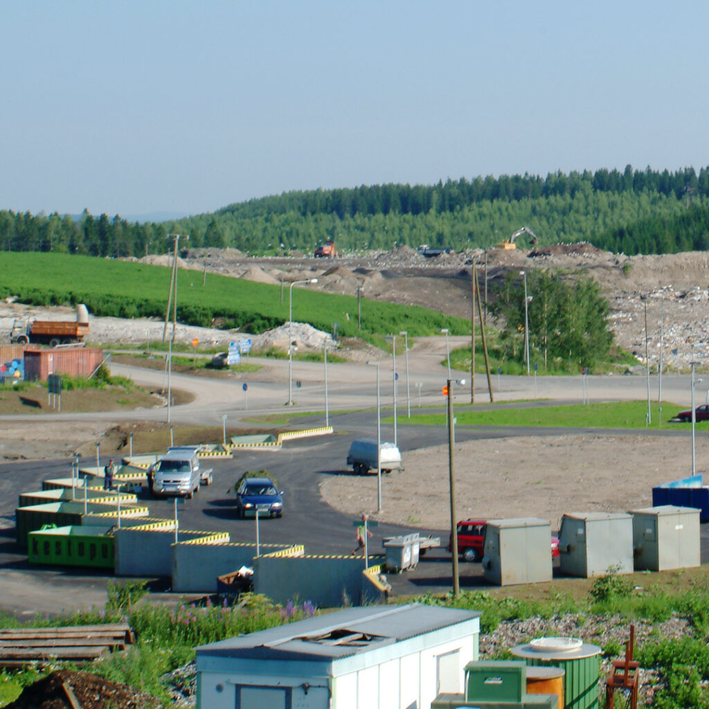 Lajittelupihalla on autoja ja ympärillä näkyy metsäistä maisemaa. Kuva on vähän vanha.